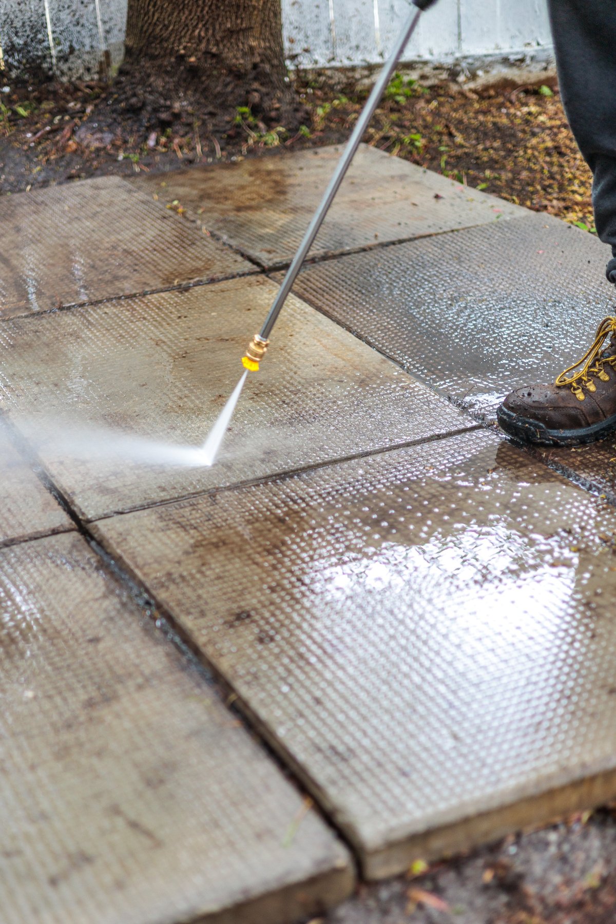 Person pressure washing a wooden deck with high-pressure water spray